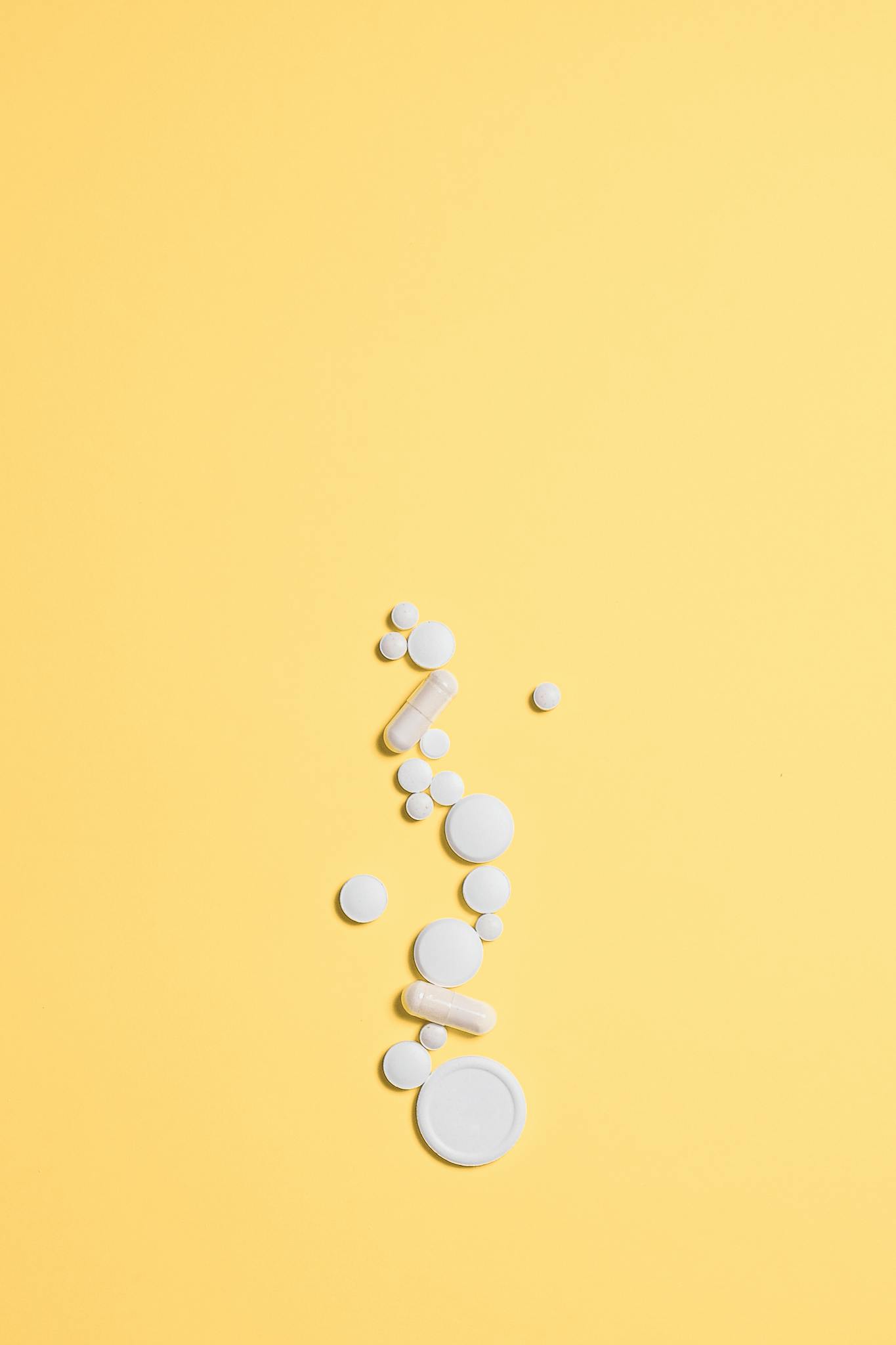 Minimalist image of white pills scattered on a vibrant yellow background, ideal for healthcare themes.